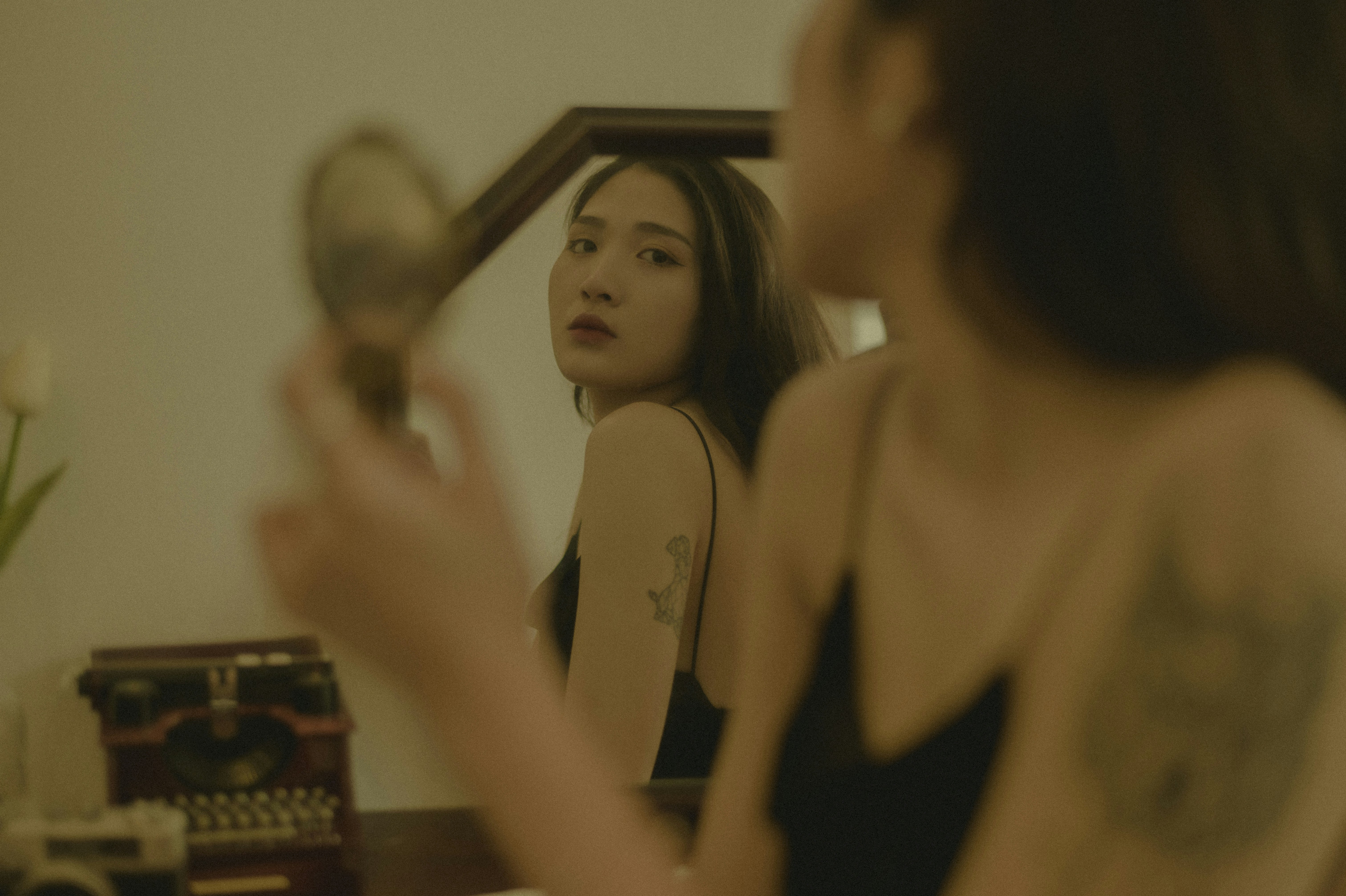 Young woman with tattoos examines her reflection in a mirror.